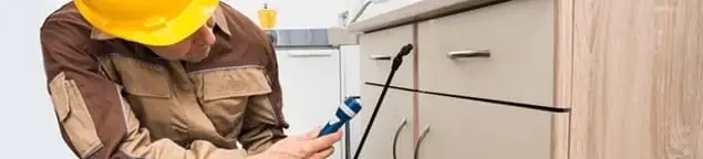 Roach exterminator applying treatment under kitchen cabinets in Reno, NV