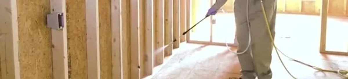 Termite treatment technician applying spray along framing and unfinished walls in Reno, NV